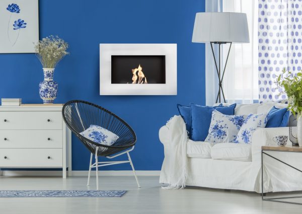 Blue and white cozy living room with decorations and a comfortable white sofa with pillows standing by a big window of a bright interior with wooden floor